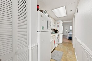 A narrow hallway with a kitchen area featuring white cabinetry, a refrigerator, and a microwave. - Bridgewater 427 Beautiful Renovated condo in Litchfield by the Sea! (Pawleys Island)