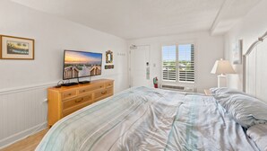 Ein Schlafzimmer mit einem Bett, einem Schminktisch, einem Fernseher und einem Fenster mit Jalousien.