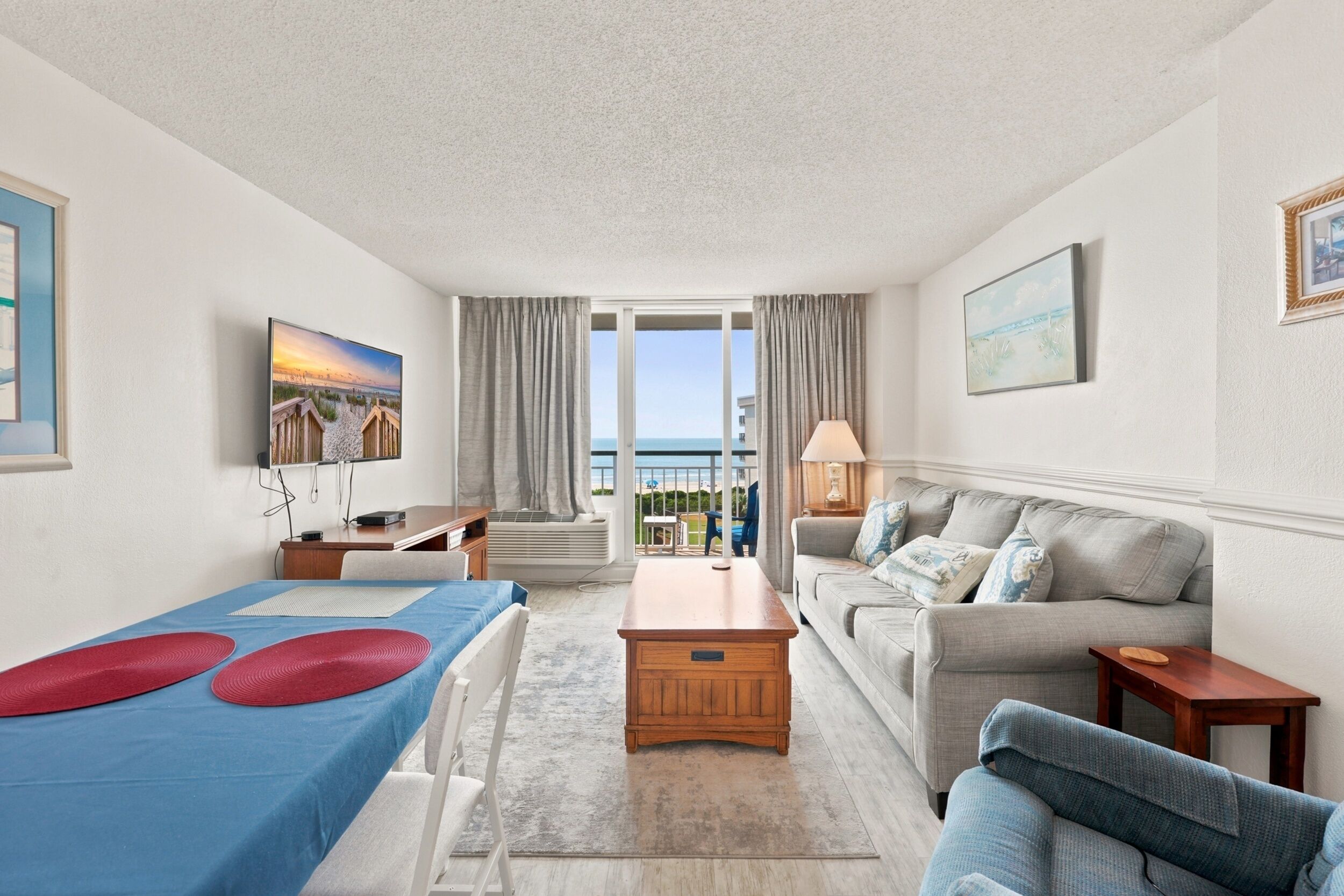 A hotel room with a bed, a sofa, a desk, a TV, and a view of the sea.