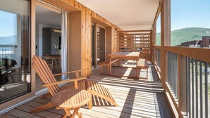 A wooden deck with outdoor furniture, a glass door leading to a room, and a view of a green landscape. - Prato - Terrace | Spa | Mtn views | Alpe d'Huez (Huez)