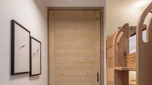 A hallway with a wooden door, framed artwork, a wooden bunk bed, and a hanging light fixture. - Prato - Terrace | Spa | Mtn views | Alpe d'Huez (Huez)