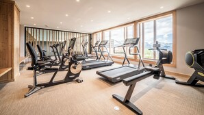 A modern gym with various cardio machines, large windows, and a view of mountains. - Prato - Terrace | Spa | Mtn views | Alpe d'Huez (Huez)