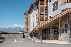 A modern hotel with a stone facade, wooden balconies, and a mountain view. - Altis - Terrace | Spa | Ski locker | Alpe d'Huez (Huez)
