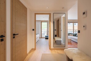 Un intérieur moderne avec une porte en bois, un couloir menant à un espace de vie comprenant un canapé et offrant une vue sur l’extérieur.