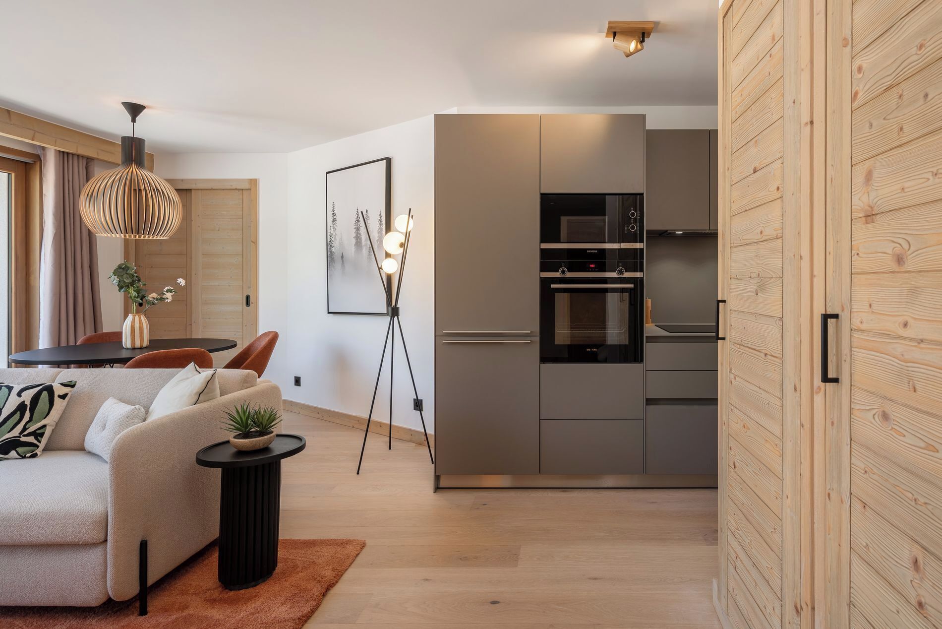 A modern kitchen with a built-in oven and microwave, a dining area with a table and chairs, and a living room with a sofa and a small side table.