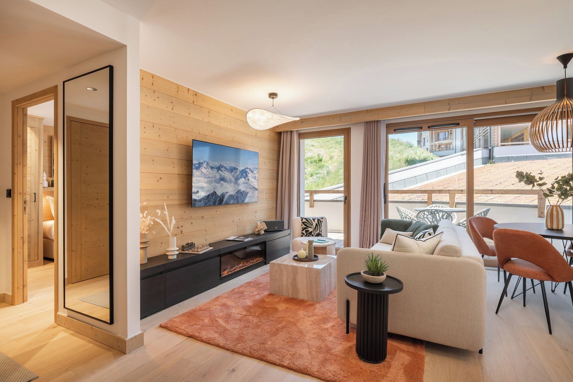 Ein modernes Wohnzimmer mit großem Fernseher, Kamin, Sofa und Essbereich mit Blick auf einen Strand.