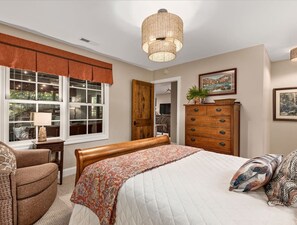 Ein Schlafzimmer mit einem Bett, einem Schminktisch, einem Stuhl, einem Fenster mit Vorhängen und einer Hängeleuchte.