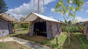 Two bamboo-framed tents with open sides, a stone pathway, and a tall communication tower in the background.