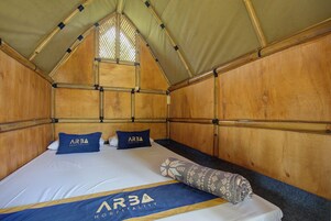A single bed with a blue and gold AR3A Hospitality logo, two matching pillows, and a patterned throw blanket.