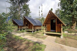 Two wooden cabins with sloped roofs, surrounded by greenery and a dirt path.