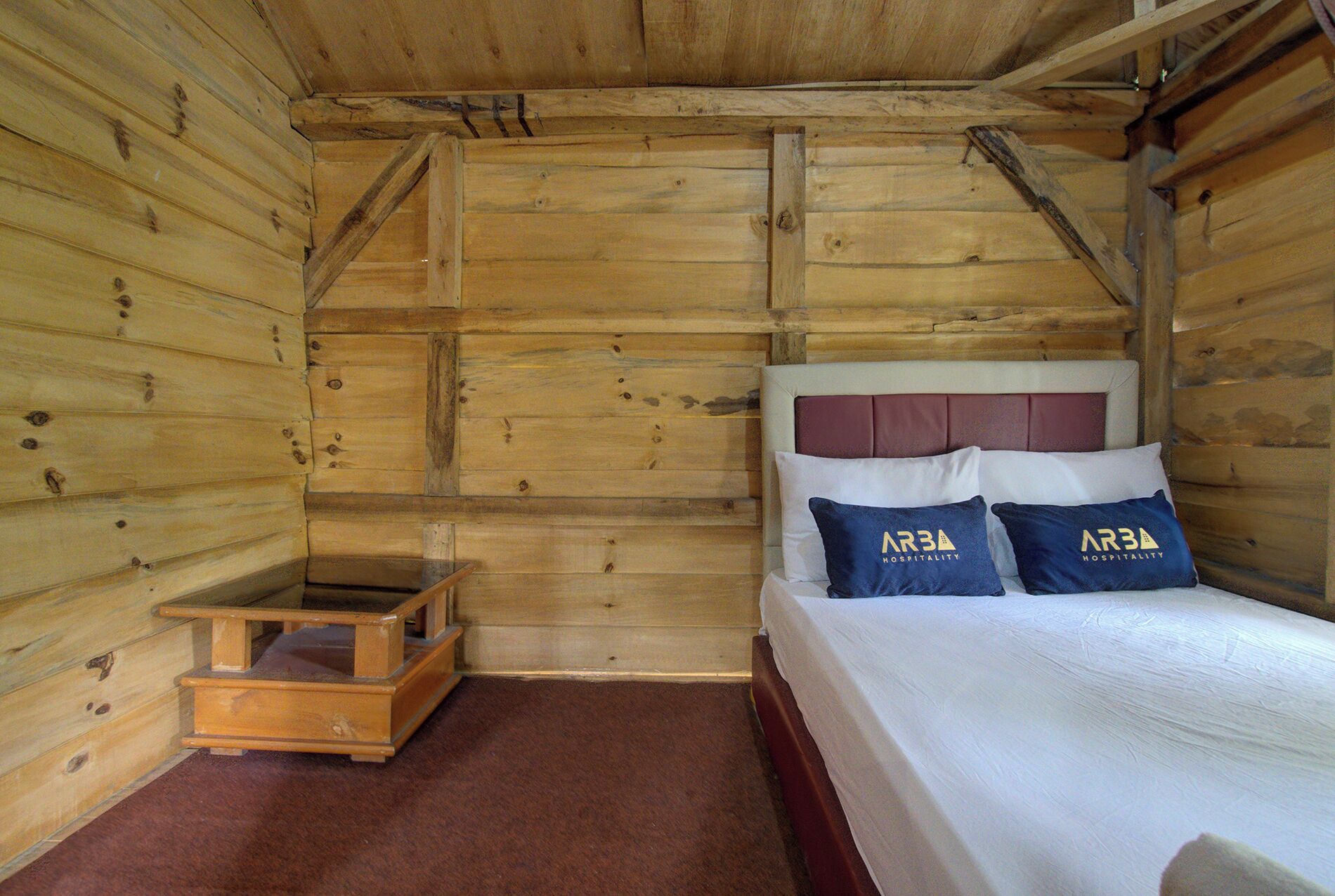Une pièce dans une cabane en bois, avec un lit, des oreillers et une petite commode en bois.