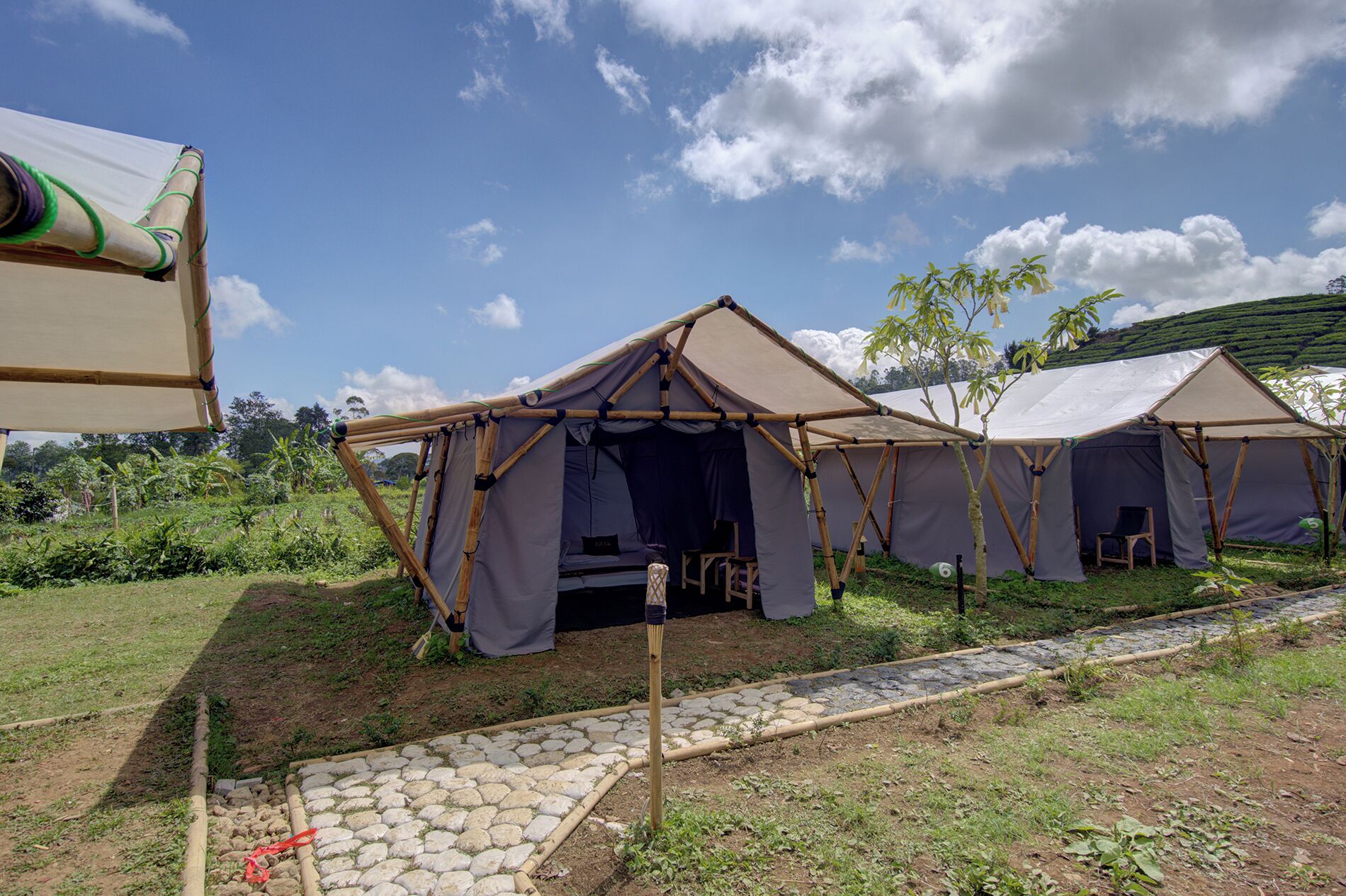 A series of tents with a stone pathway leading to them, set in a lush green area with a clear sky.
