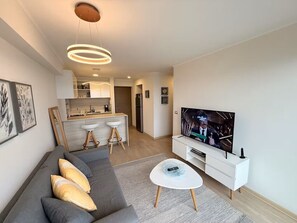 A modern living room with a sofa, a coffee table, a TV, and a kitchen area in the background. - Ocean View 2BR Pool & Gym Barranco-Miraflores (Lima)