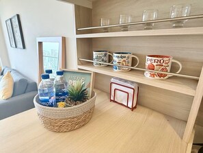 A room with a wooden shelf holding decorative mugs, a woven basket with water bottles, and a framed picture with text. - Ocean View 2BR Pool & Gym Barranco-Miraflores (Lima)