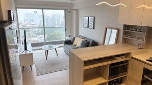 A modern apartment with a living area, kitchen, and large windows offering a city view. - 2-bedroom apartment w/ sunset view - Pool - Gym, beautiful Barranco y Miraflores (Lima)