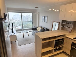 A modern apartment with a living area, kitchen, and large windows offering a city view. - 2-bedroom apartment w/ sunset view - Pool - Gym, beautiful Barranco y Miraflores (Lima)