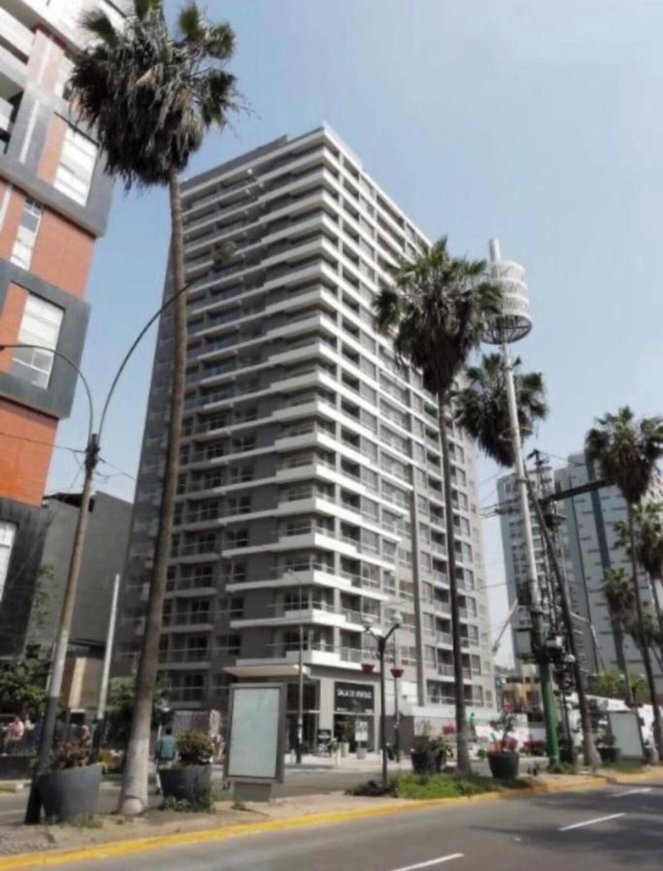 A high-rise building with multiple floors, surrounded by palm trees and other urban structures.