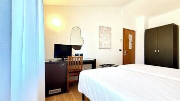 Una camera d'albergo con un letto, una scrivania con un computer, una sedia, un armadio e un'opera d'arte appesa al muro.