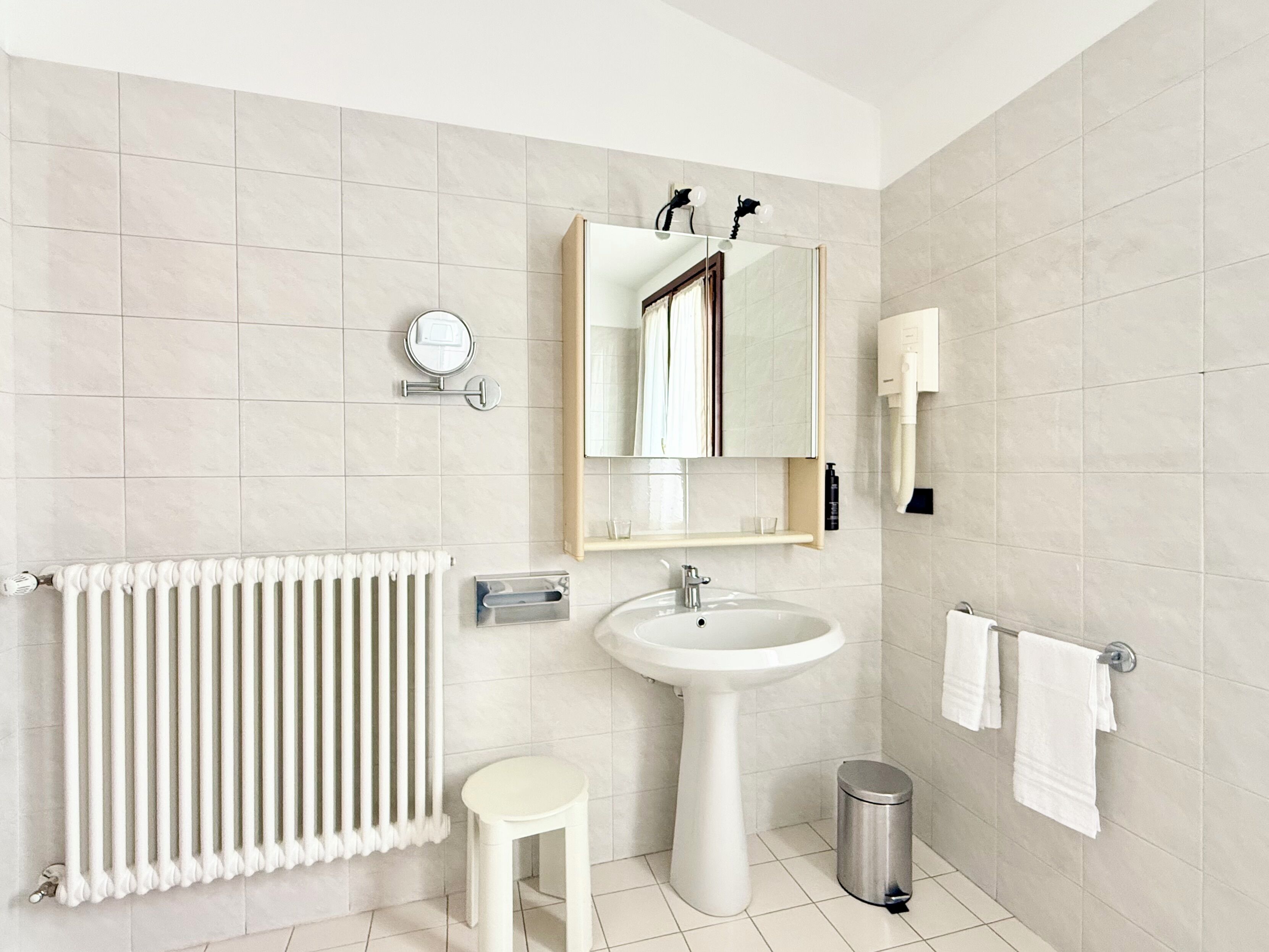 Een moderne badkamer met een witte wastafel, spiegel, handdoekrek en radiator.