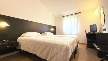 Habitación de hotel con cama, mesita de noche con teléfono, escritorio con computadora y ventana con cortinas.