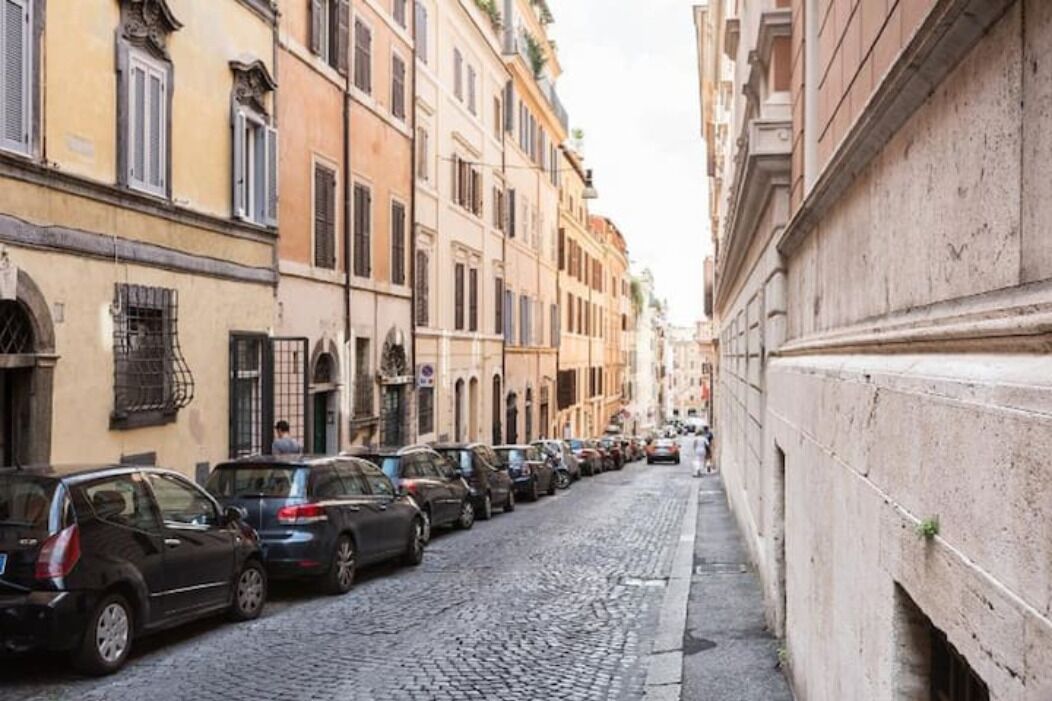 A narrow cobblestone street lined with parked cars and historic buildings.