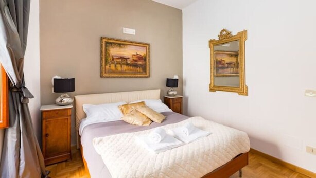 A hotel room with a bed, two bedside tables, a nightstand, a painting on the wall, and a mirror. - Rome Apartment Trevi Spagna Charme, Barberini Metro Station (Roma)