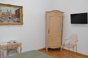 A room with a wooden cabinet, a chair, a desk with a computer, and a painting on the wall. - Rome Apartment Trevi Spagna Charme, Barberini Metro Station (Roma)