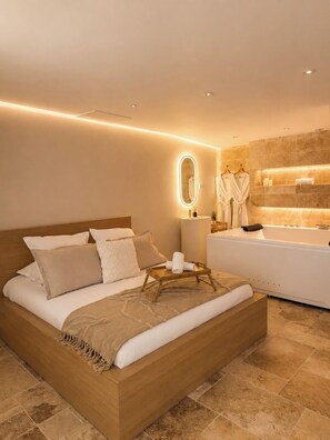 A modern bedroom with a large bed, a bedside table, a mirror, and a bathroom with a bathtub and towels. - L'Escapade (Le Mans)