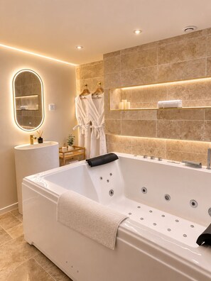 A modern bathroom with a freestanding bathtub, a mirror with integrated lighting, and a towel rack with robes. - L'Escapade (Le Mans)