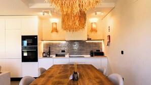 A modern kitchen with a wooden dining table, built-in appliances, and a hanging light fixture. - MyStay - Aunt Olinda (Porto Covo)
