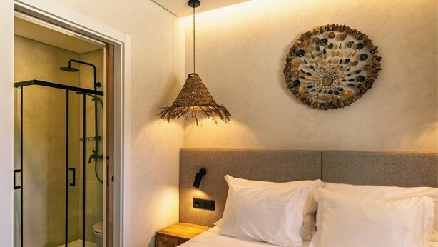 A hotel room with a bed, a wall-mounted decorative item, a hanging light fixture, and a shower area. - MyStay - Aunt Olinda (Porto Covo)