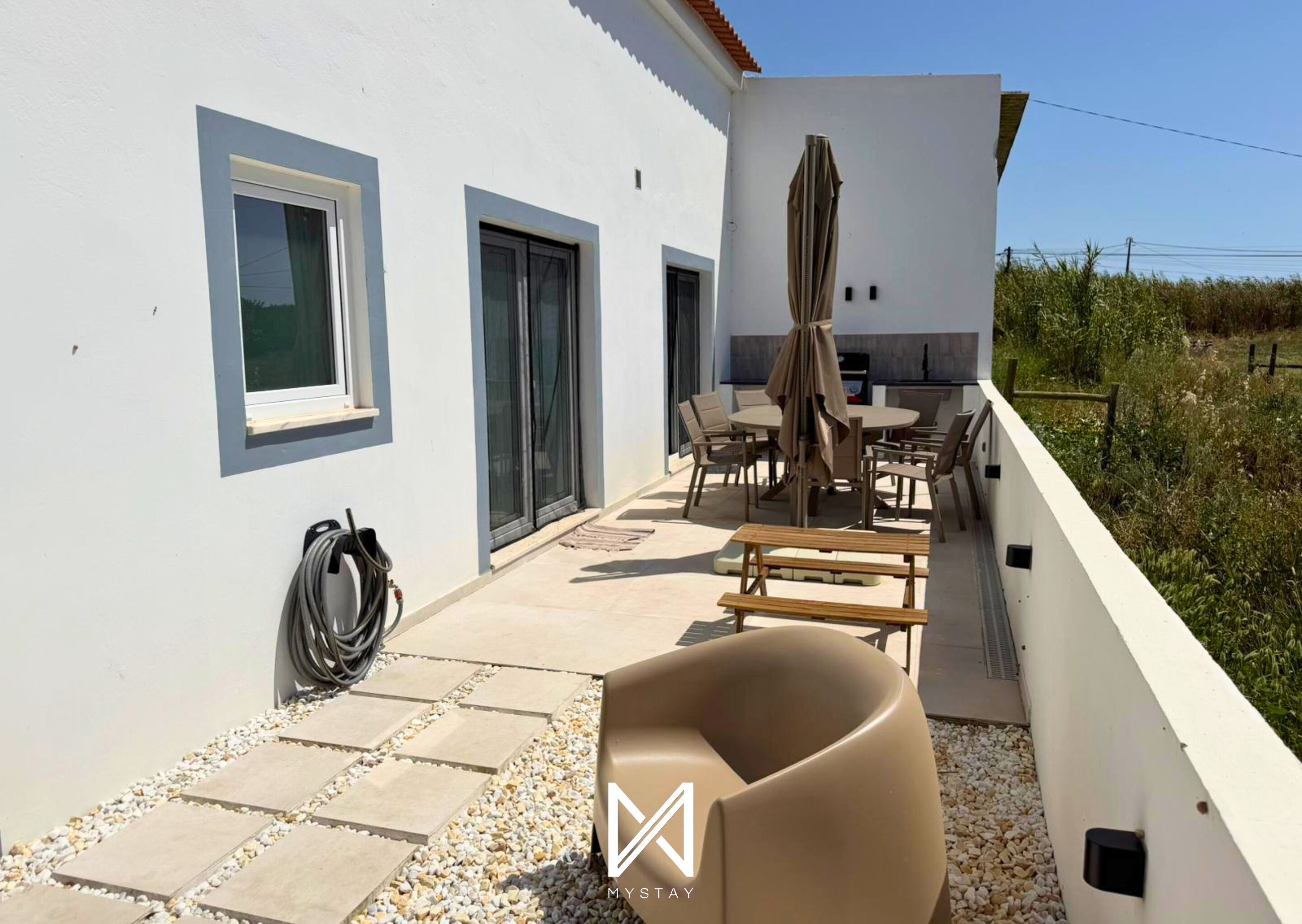 A modern outdoor patio with a dining area, a barbecue grill, and a water hose.