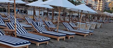 A beach with rows of wooden lounge chairs and white umbrellas.