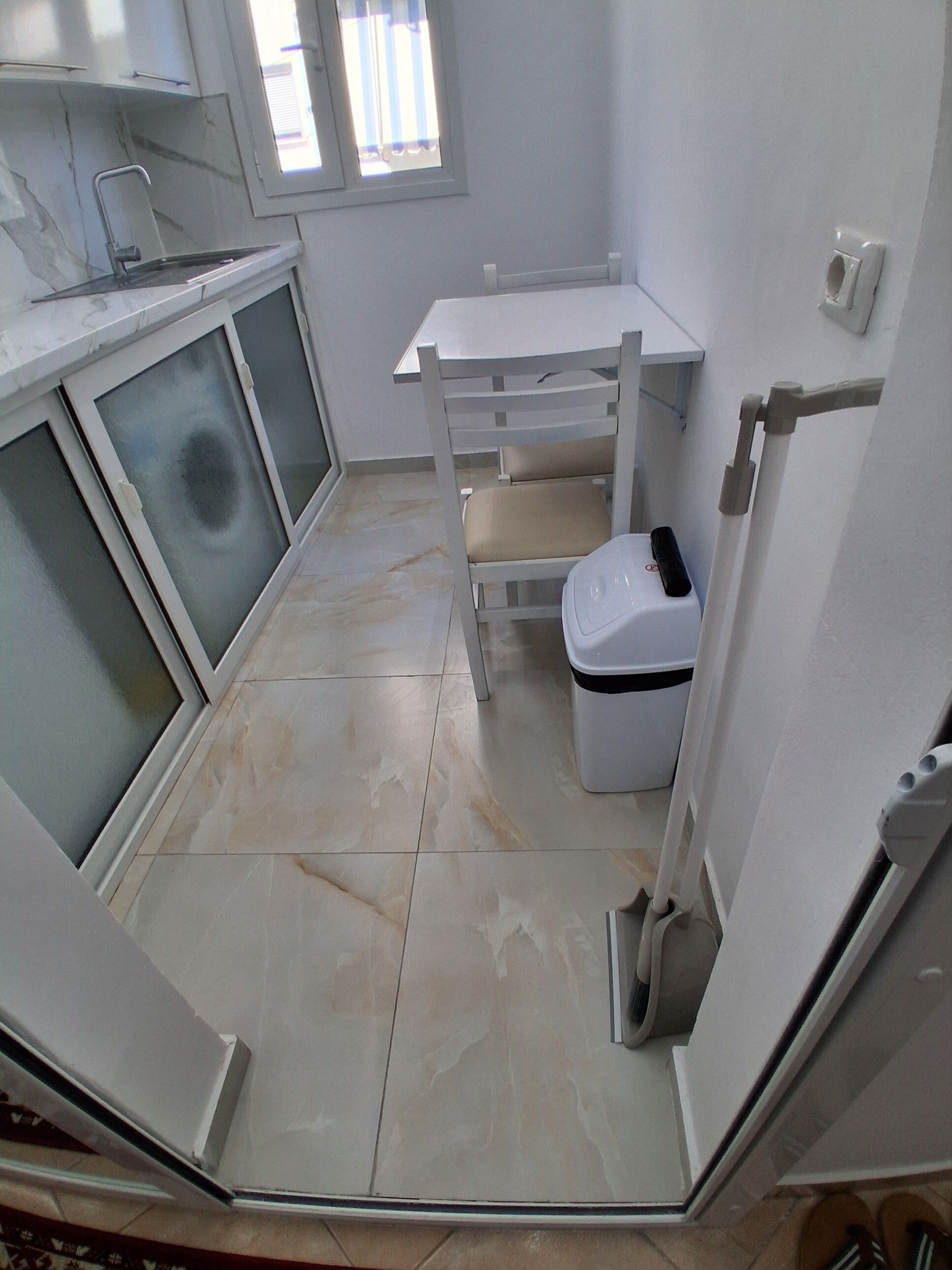 A compact kitchen with a white countertop, a sink, a trash bin, and a window.
