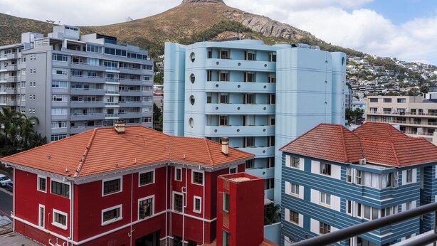 A multi-story building with a red and blue facade, a prominent mountain in the background, and a clear sky. - Dolce Vita | Luxury 3 bed Retreat (Cape Town)
