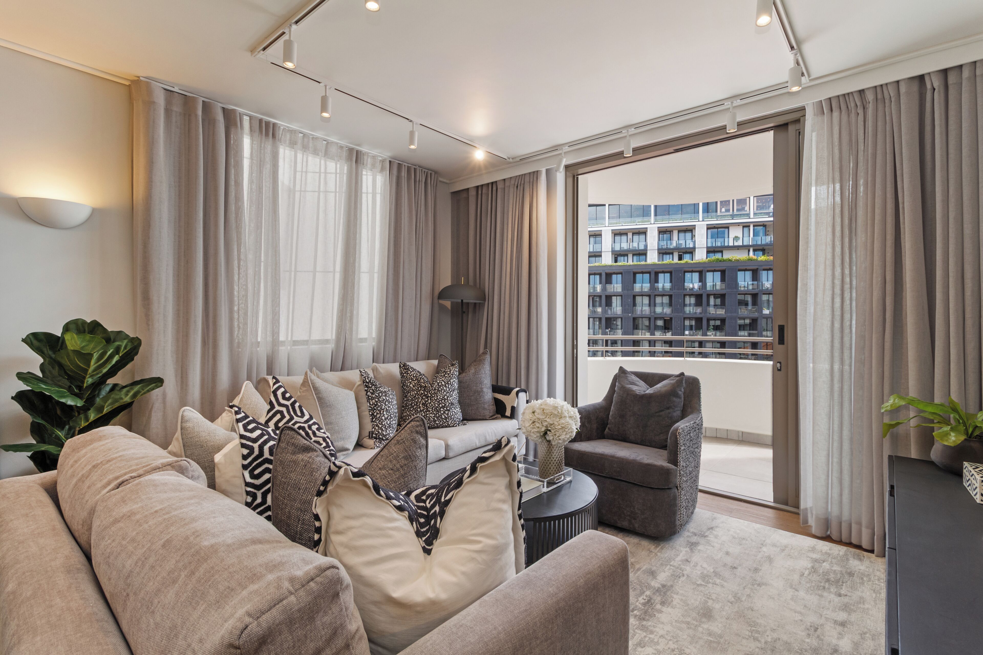 Een moderne woonkamer met een bank, fauteuils, een salontafel en uitzicht op een gebouw door een groot raam.
