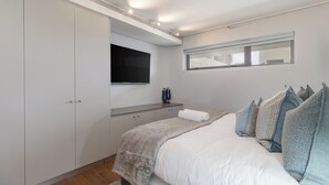 A bedroom with a bed, a TV mounted on the wall, a wardrobe, and a window. - Dolce Vita | Luxury 3 bed Retreat (Cape Town)