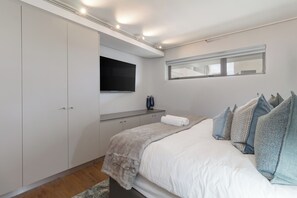 Ein Schlafzimmer mit Bett, einem an der Wand befestigten Fernseher, einem Kleiderschrank und einem Fenster.