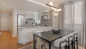 A modern kitchen with a central island, a dining area with a dark table, and a living space with a large window. - Dolce Vita | Luxury 3 bed Retreat (Cape Town)