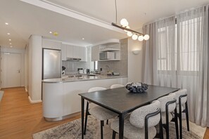 Eine moderne Küche mit Kochinsel, ein Essbereich mit dunklem Tisch und ein Wohnbereich mit großem Fenster.