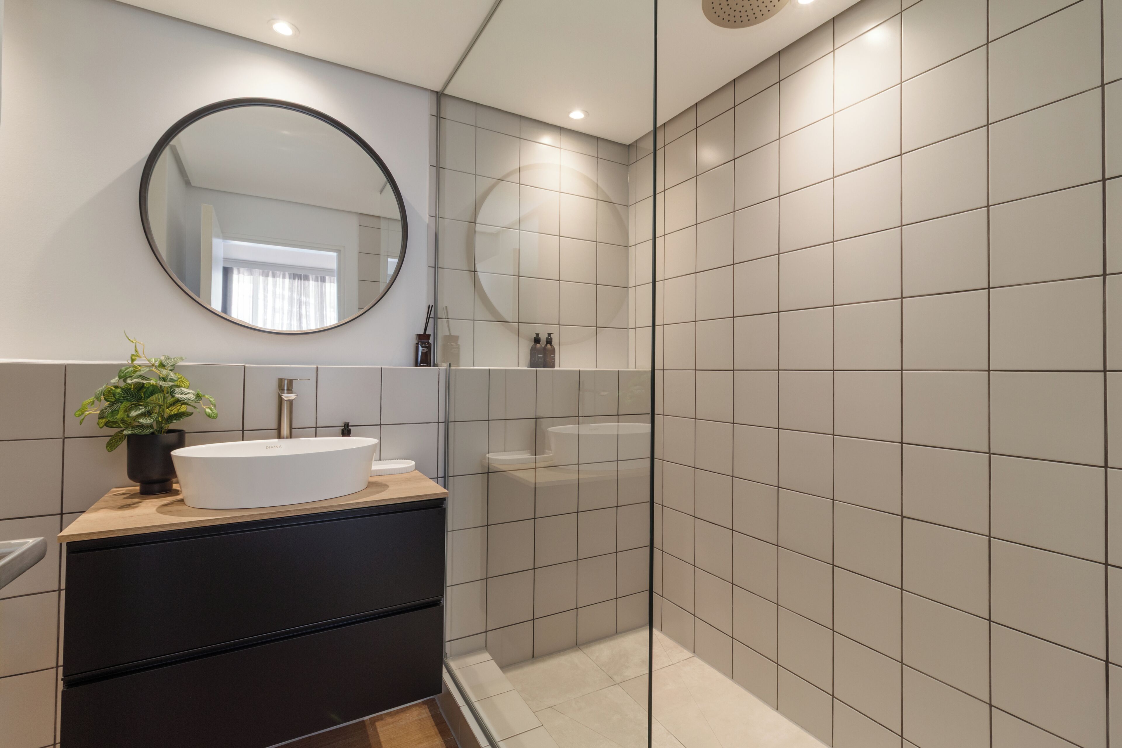 Een moderne badkamer met een ronde spiegel, een wastafel, een plant in pot en een douche.