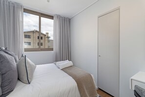 A hotel room with a bed, a window with curtains, a door, and a view of a building outside. - Dolce Vita | Luxury 3 bed Retreat (Cape Town)