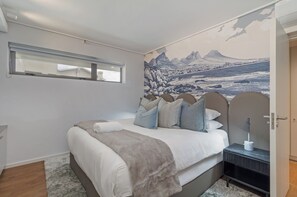 Ein Schlafzimmer mit Bett, Nachttisch, Fenster und Wandbild.