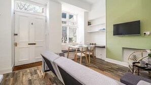 Una sala de estar moderna con un banco, una mesa de comedor con sillas, un televisor de pantalla plana montado en la pared y una ventana con persianas.