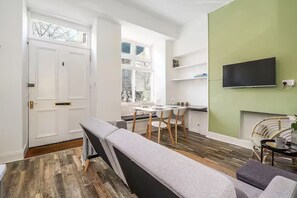 A modern living room with a bench, a dining table with chairs, a flat-screen TV mounted on the wall, and a window with blinds. - Modern - 2BR Flat near Easter Road Stadium (Edinburgh)