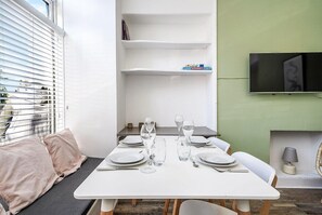 A dining area with a white table set for four, glasses, plates, and cutlery. There are shelves above the table and a television mounted on the wall. - Modern - 2BR Flat near Easter Road Stadium (Edinburgh)
