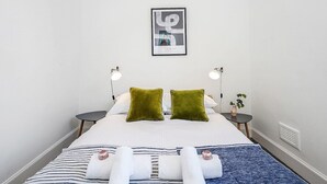 Habitación de hotel con una cama, dos mesitas de noche, un cuadro en la pared y una planta pequeña en una de las mesitas.