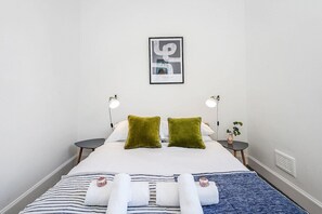 A hotel room with a bed, two bedside tables, a framed picture on the wall, and a small plant on one of the tables. - Modern - 2BR Flat near Easter Road Stadium (Edinburgh)