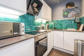 A modern kitchen with a microwave, toaster, and oven, a sink, and a first aid kit on the wall. - Modern - 2BR Flat near Easter Road Stadium (Edinburgh)