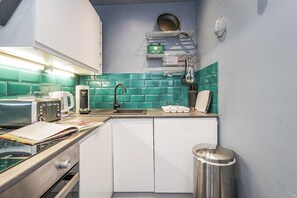Cocina compacta con lavamanos, estufa y microondas. Hay un botiquín en la pared y un cubo de basura.